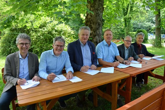 Sechs Männer unterzeichnen am Tisch einen Vertrag.
