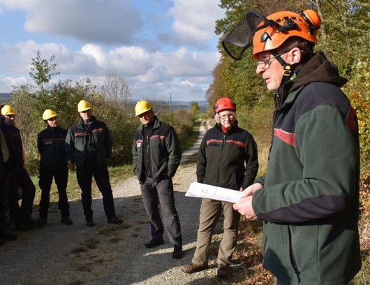 Forstleute vor einem Waldstück, die einem Vortragenden lauschen.