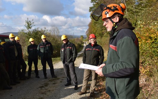 Forstleute vor einem Waldstück, die einem Vortragenden lauschen.
