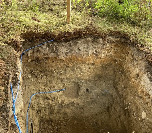 ausgehobenes Loch mit Messinstrumenten im Waldboden