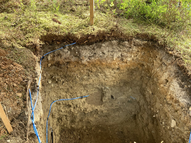 ausgehobenes Loch mit Messinstrumenten im Waldboden