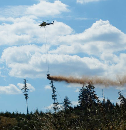 Kalk wird vom Hubschrauber aus über einem Wald verstreut.